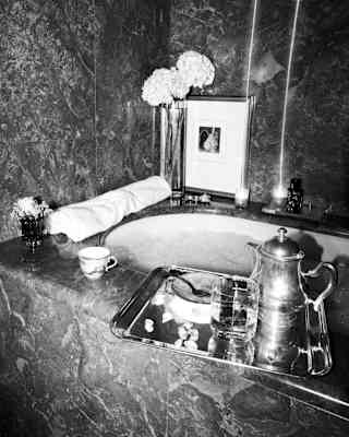 A relaxing bath full of bubbles awaits, with flowers and lit candles on its marble-topped edges, and a silver tray of supper