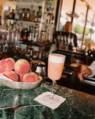 A pink Peach Bellini cocktail rests on a napkin next to a bowl of peaches on the green marble bar top at Il Bar Gabbiano.