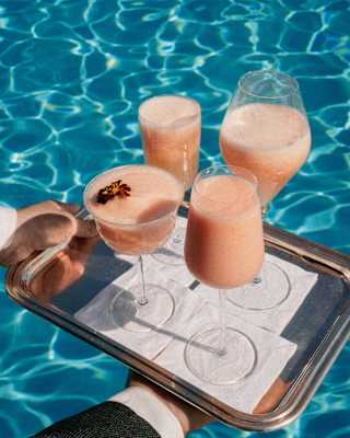 Close-up on a tray of Peach Bellini cocktails served in four different-shaped glasses with a shimmering pool-water backdrop.
