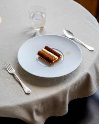 A chocolate dessert comprising three tubes with blankets of cocoa and gold leaf, served at Oro restaurant, seen in close-up.