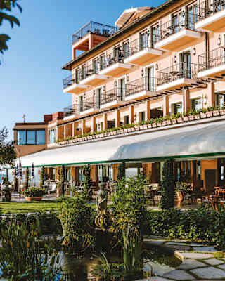 Garden pond with a classical statue in the middle and a grand coral-coloured hotel facade behind