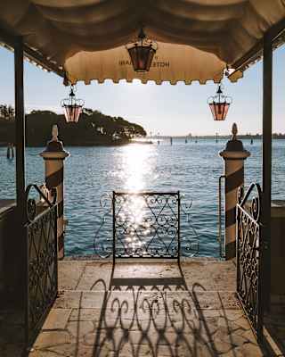 View of the glittering Venetian Lagoon along a stone pier with an awning and rose glass lanterns