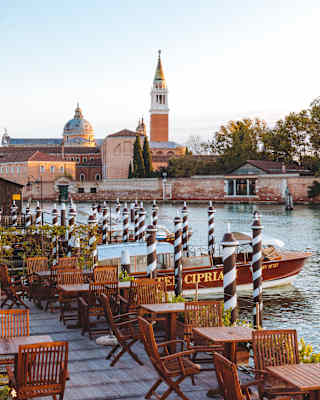Wooden cafe tables on a terrace beside the Venetian Lagoon with views of St Mark's Square
