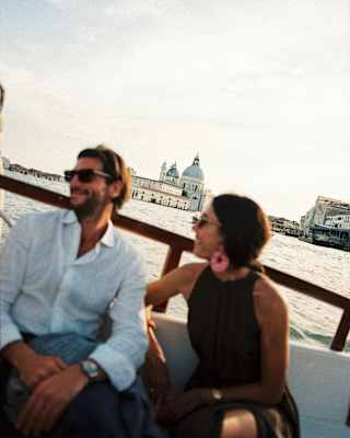 Tilted image of a man and woman in soft-focus as they relax on a boat, with the Basilica di Santa Maria della Salute crisp behind.