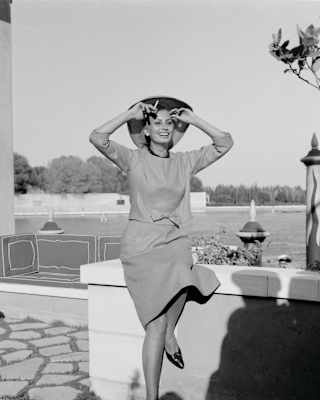 A black and white image of Italian actress, Sophia Loren, smiling as she sits on a low wall in grounds of the Hotel Cipriani