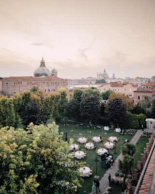 Circular banquet tables on a manicured lawn surrounded by trees in the heart of Giudecca, Venice
