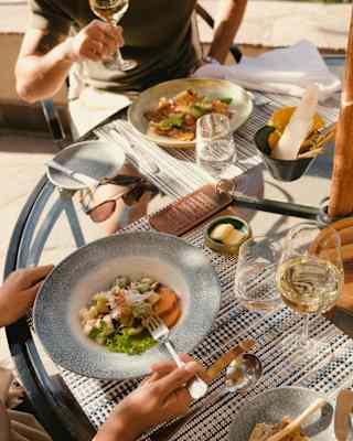 Guests enjoy a fresh light lunch with white wine, seen from above, close-up, at a sunny al fresco table at Curiña Restaurant.