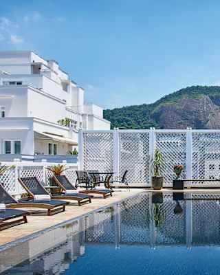 A black-tiled penthouse pool reflects a mountain in its still water. White trellis and green hedging surrounds the deck