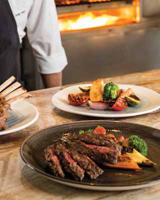 A chef adds the final garnish to charcoal grilled beef ribs and Angus steaks with a side plate of grilled vegetables