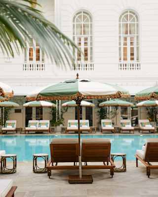 Cream and sage parasols stand to attention beside teak sun loungers that lie ready for guests around a turquoise pool