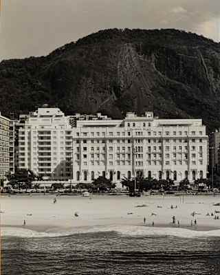 A vintage image of the hotel's facade and beach with the forested mountain behind shows almost no difference to today