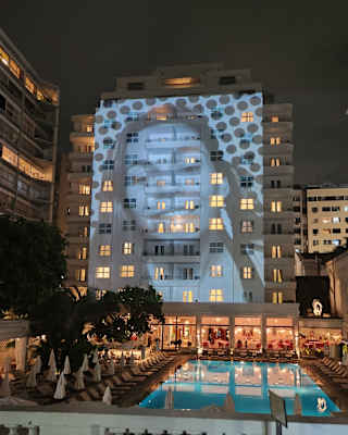 The face of a smiling woman is projected on the hotel façade at night, by artist JR and Casa Amarela for Mother's Day.