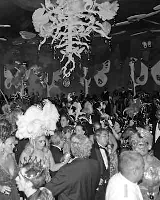 Giant butterflies hang from the ceiling and walls. Party-goers in carnival costumes and black tie fill the ballroom and dance