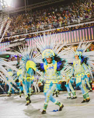 Carnival dancers, in flamboyant feather headdresses and yellow ad blue costumes, dance for an audience at the Sambadrome.