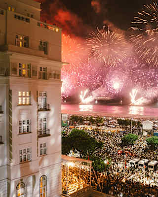 People crowd the streets outside Copacabana Palace to celebrate New Year as pink and gold fireworks spray the night sky.