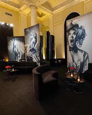 View of a lounge with black banquettes and tables with candles, and large panels with monochrome photographs of entertainers.