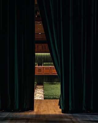 Peering through a gap in the green velvet curtains we can see from the stage to the stalls, wood panelling and green seating