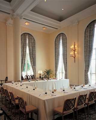 Meeting tables are set in a horseshoe shape with individual water and notepads. Cathedral height arched windows add drama