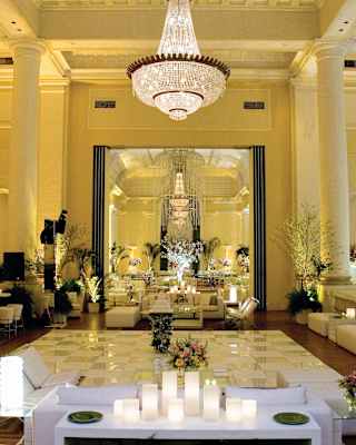 An Art Deco chandelier hangs in the Gallery Room where plants and lights warm white décor, reflected in a huge wall mirror.