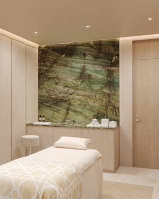 A bed awaits a client in a bright, wood-panelled Dior Spa room with a sofa and a basin unit with a green marble feature wall.