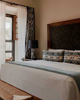 Terrace doors bring light into a Deluxe Room, with a white bed with blue-patterned fabrics, and natural wood and tile décor.