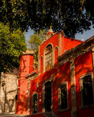 View of the fortress-style mansion, Casa Parque, with vivid red rendering and stone, brushed by shadows from nearby trees.