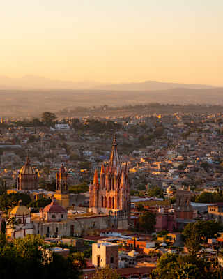 Aerial view over San Miguel de Allende in sunset light with the pink stone of Parroquia San Miguel Arcángel glowing rose-gold.