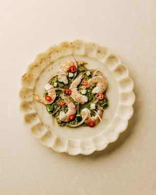 Prawn Aguachile with prawns on a lime and leaf base with red chillies, served on a scallop-edged plate, seen from above.