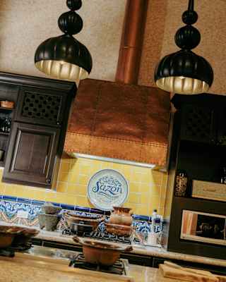 Angled image of a homely kitchen with black pendant lights, copper extractor, traditional tiles and wall-mounted Sazon plate.