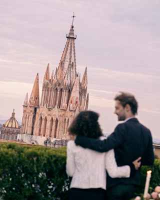 Tilted soft-focus image of a couple arm in arm, seen from behind as they face the iconic rose-hued church with gothic spires.