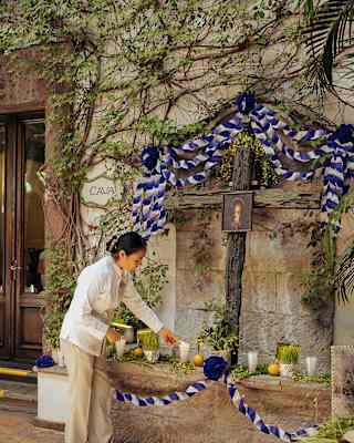 A woman lights a candles at a wall shrine with a wooden cross and a religious picture adorned with a blue and white ribbon.