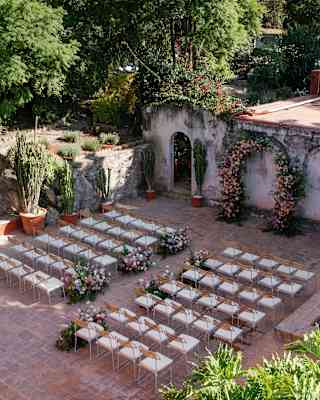 Inside the open, stone-walled, terracotta Cactus Terrace, guest aisle seating faces a rose wedding arch, seen from above.