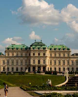 Visitors walk the grounds of the baroque Upper Belvedere Palace, with green copper octagonal, mansard, and domed roofs.