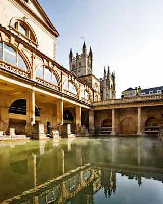 Open-air Roman bath surrounded by sandstone columns under blue skies