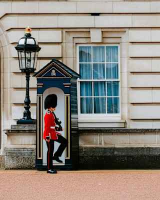 A Queen's guard, in a red uniform a bearskin hat, marches outside his sentry box, holding a rifle, seen at Buckingham Palace.