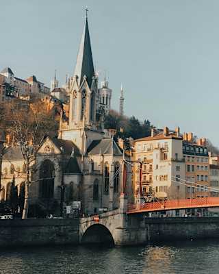 The red Passerelle Saint-Vincent bridge crosses the Saône, met on the south side by the grey-spired Église Saint-Georges de Lyon.