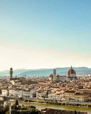 View over the river Arno to Florence's cathedral duomo, spires and belltowers which rise from a cluster of terracotta roofs.