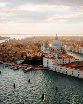 Stunning high-angle view over the Venice lagoon to Giudecca and the historic centre, terracotta roofs glowing in evening sun.
