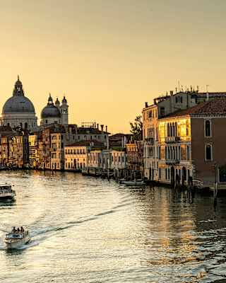 Three boats cruise the Grand Canal, leaving waves on the silvery water as a sunset honeys the sky and brushes the buildings gold.