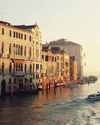 A boats cruises towards Basilica Santa Maria della Salute on the Grand Canal as morning sun glows on the waterfront buildings.