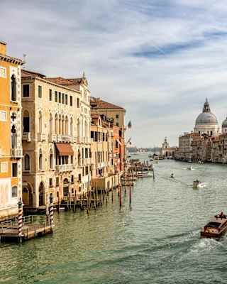 Boats cruise the greenish Grand Canal, flanked by sun-drenched Venetian houses, in a view capturing the Punta della Dogana.