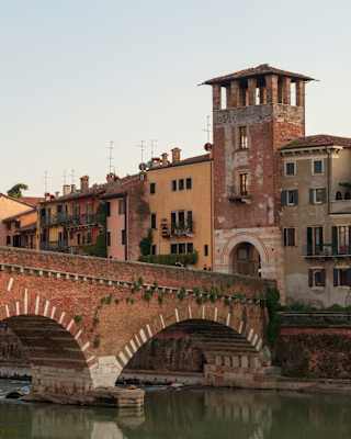 The red and white Ponte Pietra crosses Verona's Adige river, stopping at the stone archway flanked by riverside houses.