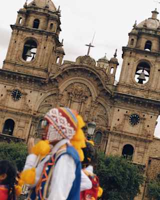 Tilted view of the Church of the Society of Jesus in Cusco, with a man in traditional clothing seen in soft-focus foreground.