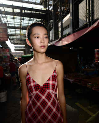 Kitajima photographs Balinese model, Echo with short dark hair, at a market wearing a strappy Marc Jacobs-style plaid dress.