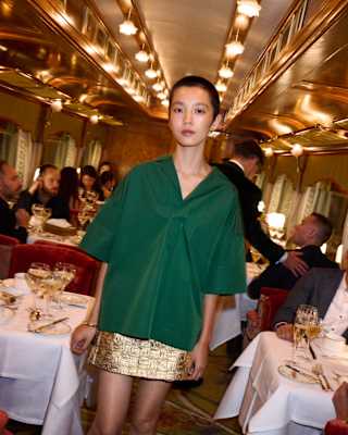 A model in a green top and gold miniskirt walks through the restaurant where every table is busy with guests, food and wine.