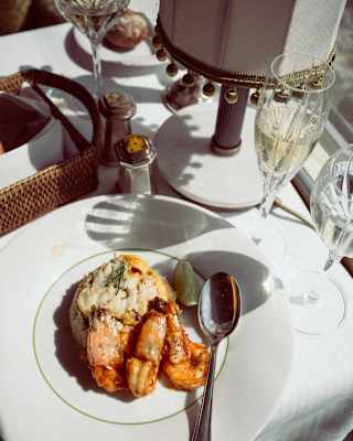 Looking down on a dish of glazed king prawns on a plate with a spoon, served with white wine in crystal glasses.