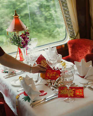 A waiter places red and gold lucky money bags on a table in Malaya Dining Car, decorated and laid for a celebration meal.