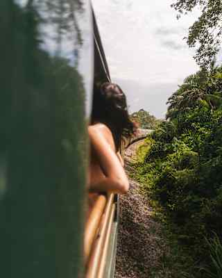 A woman's elbows jut from the train as she leans back on the rails of the Observation Deck, seen from the exterior.