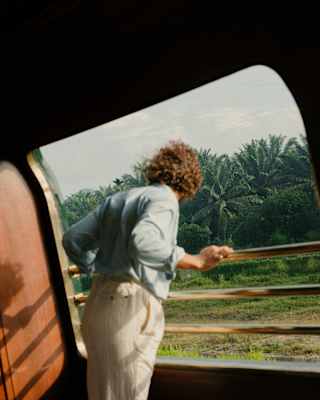 A man in white trousers and blue top leans over the Observation Deck bars, looking back at the palm-filled landscape behind.