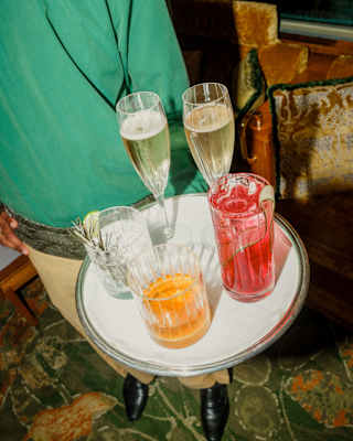 A tray with a red cocktail, a whisky tumbler, a clear spirit with rosemary sprig and two flutes of champagne, seen from above.
